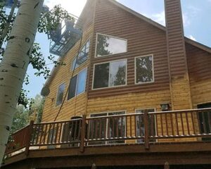 a home with wood siding being sandblasted by a professional in a lift
